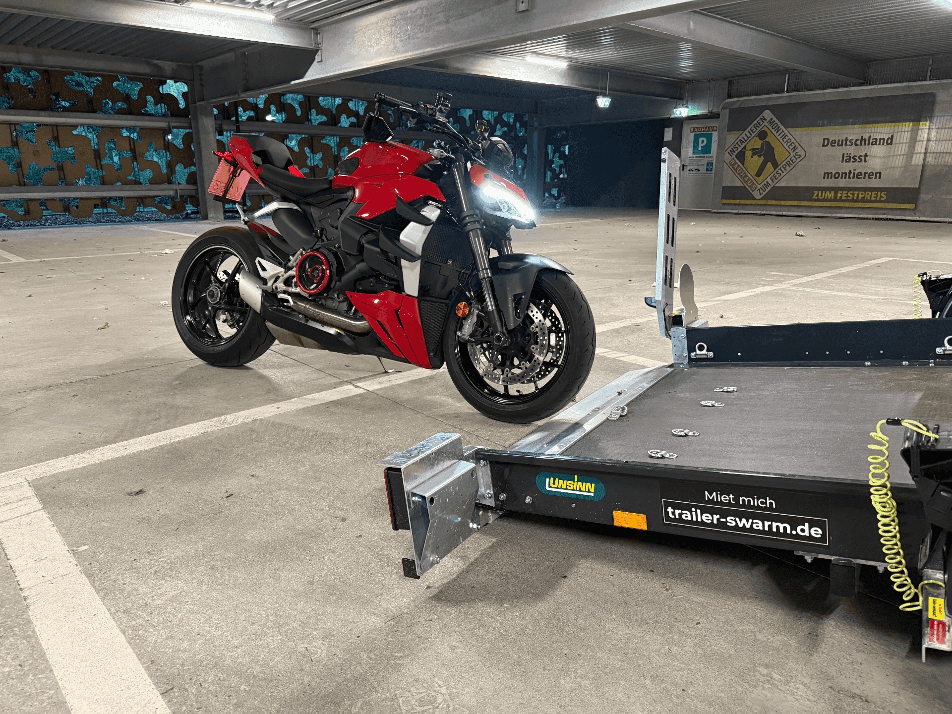 Rote Ducati Streetfighter neben einem abgesenkten Unsinn-Motorradanhänger von Trailer Swarm in einer Tiefgarage